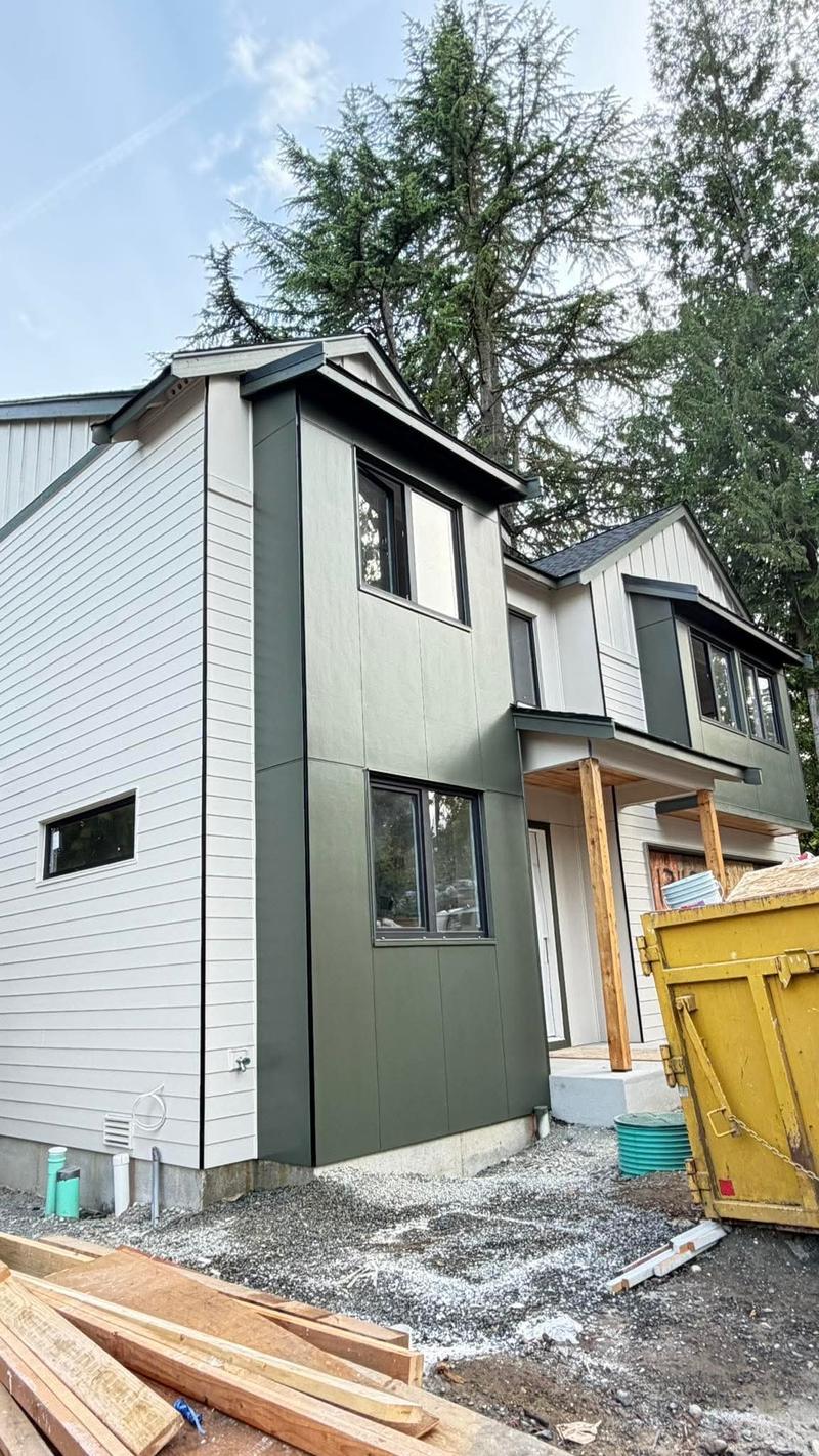 A modern two-story exterior painted olive green and off-white, with black window trim and a covered entry.