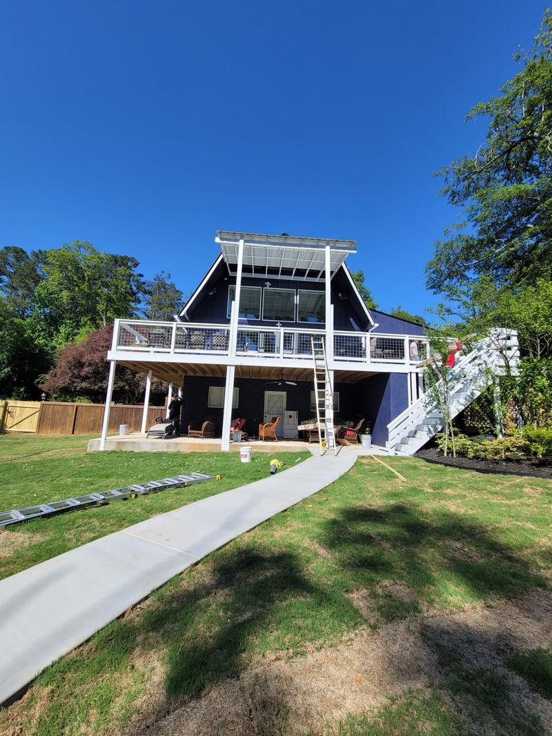 A dark navy painted house with a bright white raised deck, railings and stair rail against a clear sky.