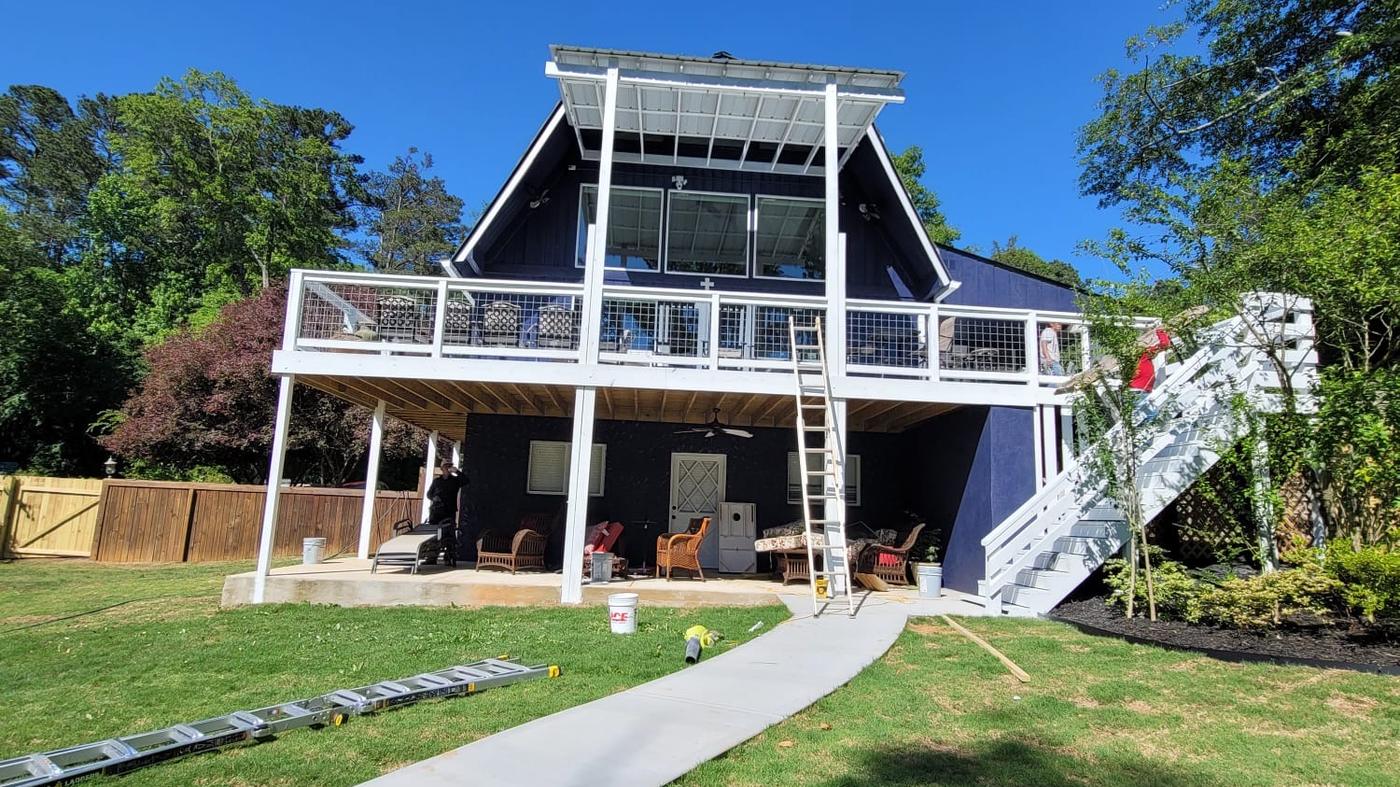 A dark navy painted house with a bright white raised deck, railings and stair rail against a clear sky.