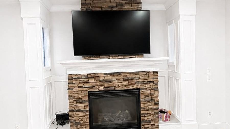 A finished living room with white painted columns and wainscot, a stone fireplace surround and light wood flooring.