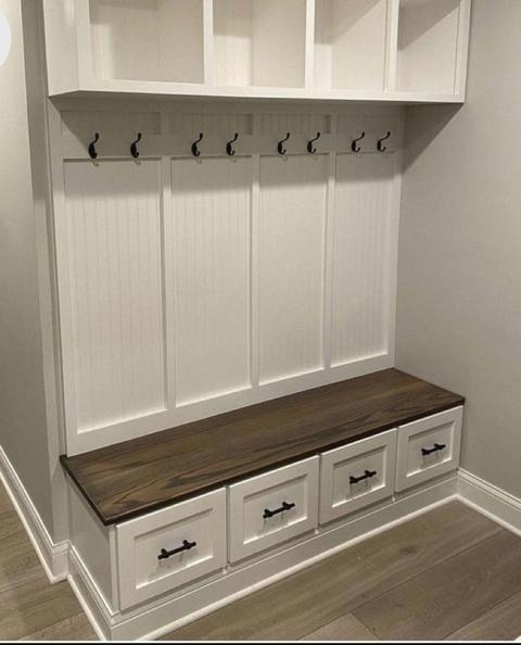 A built-in mudroom unit with white bead-board lockers, upper cubbies, coat hooks and a stained wood bench over drawers.